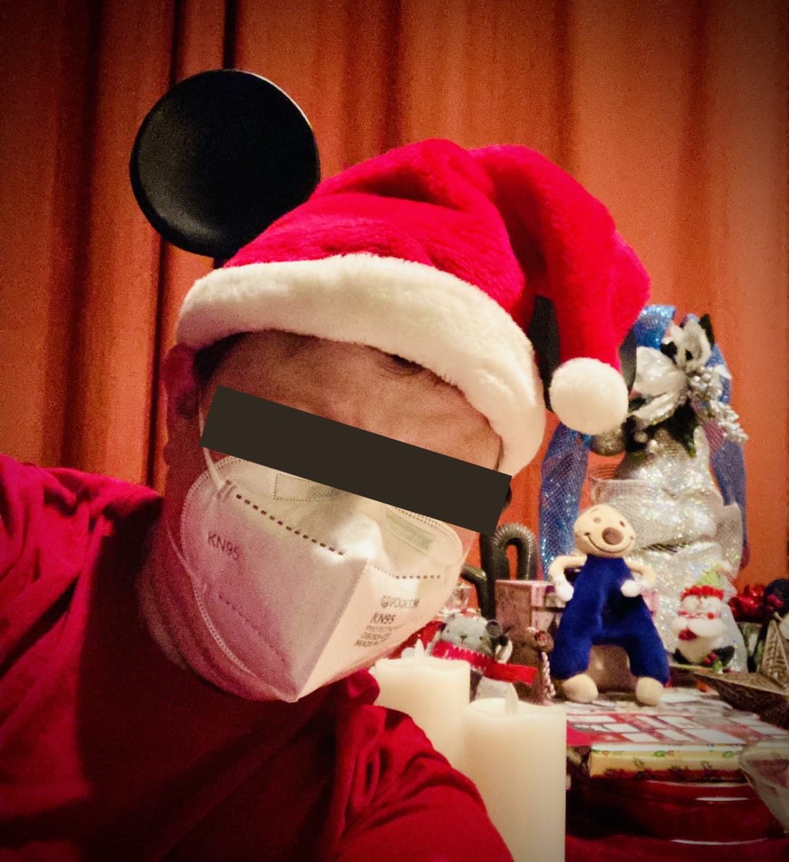 Me in a Santa Clause hat with Mickey Mouse ears, a KN95 mask, and a gray privacy bar digitally imposed across my eyes. An Andy Anaheim plushie smiles in the background.