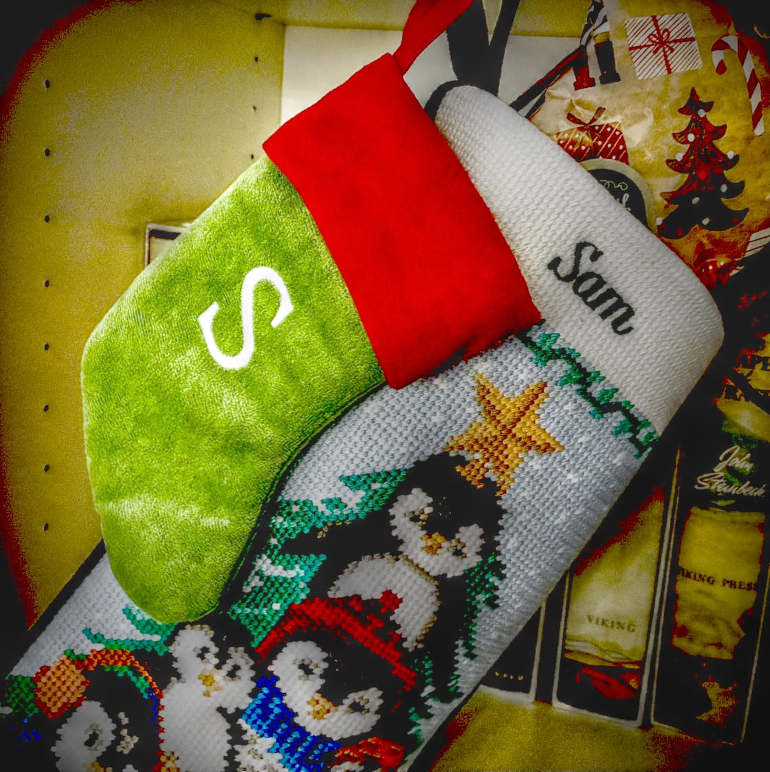Two Christmas stocking, one with just an "S" on it and another that says "Sam" hung from what's obviously a bookshelf. Steinbeck's Grapes of Wrath peaks out from behind.