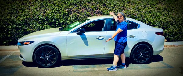 A happy woman stands, spokesmodel-style, next to a beautiful 2025 Mazda3 sedan.